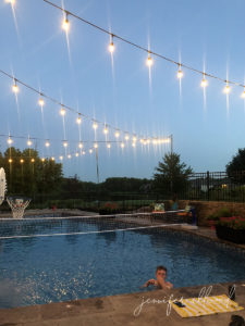 teen boy swimming in pool at dusk with string lights hung up over pool